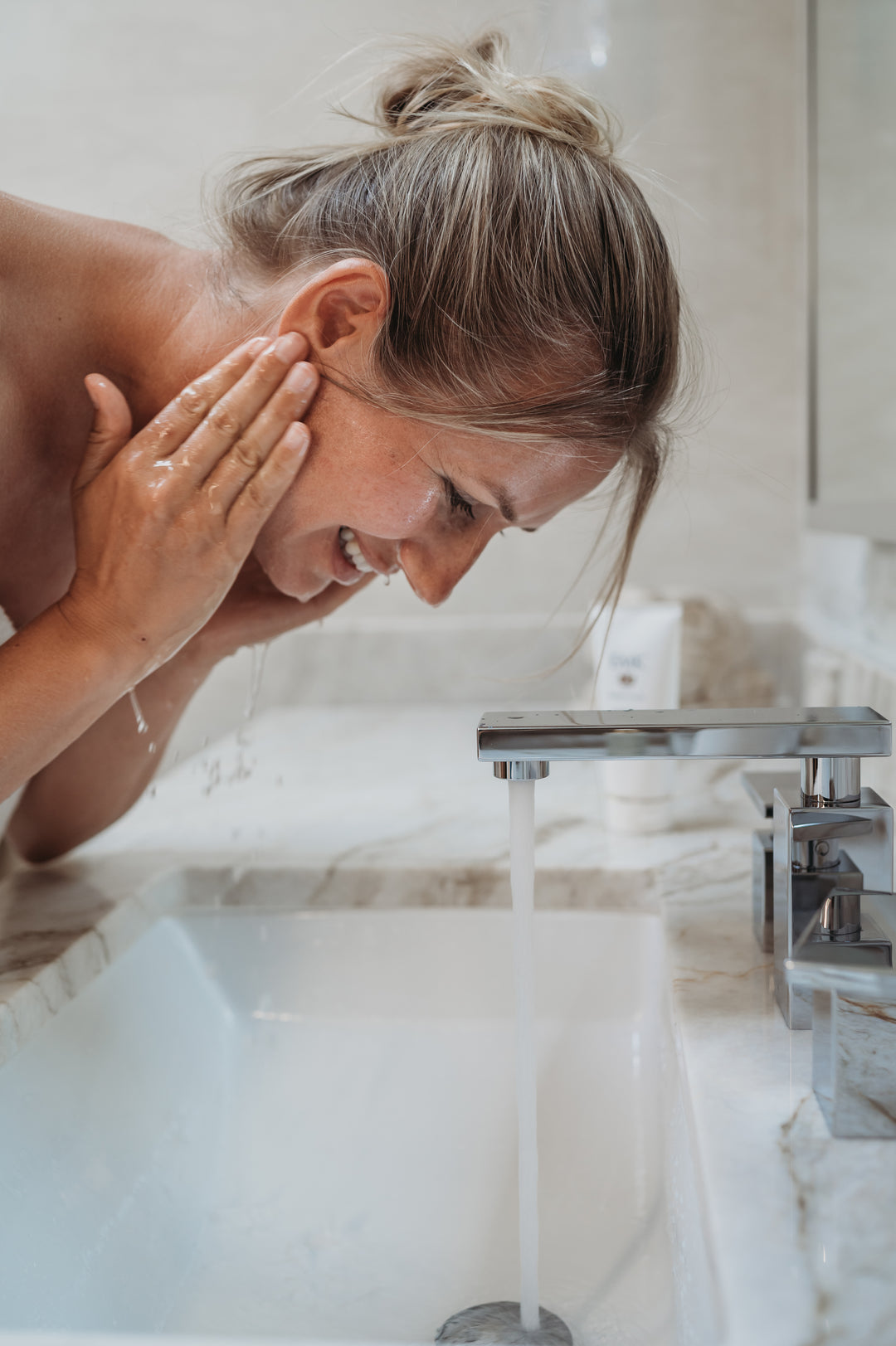 Model massaging Aurora Cleanser into cheek by EMK Skincare