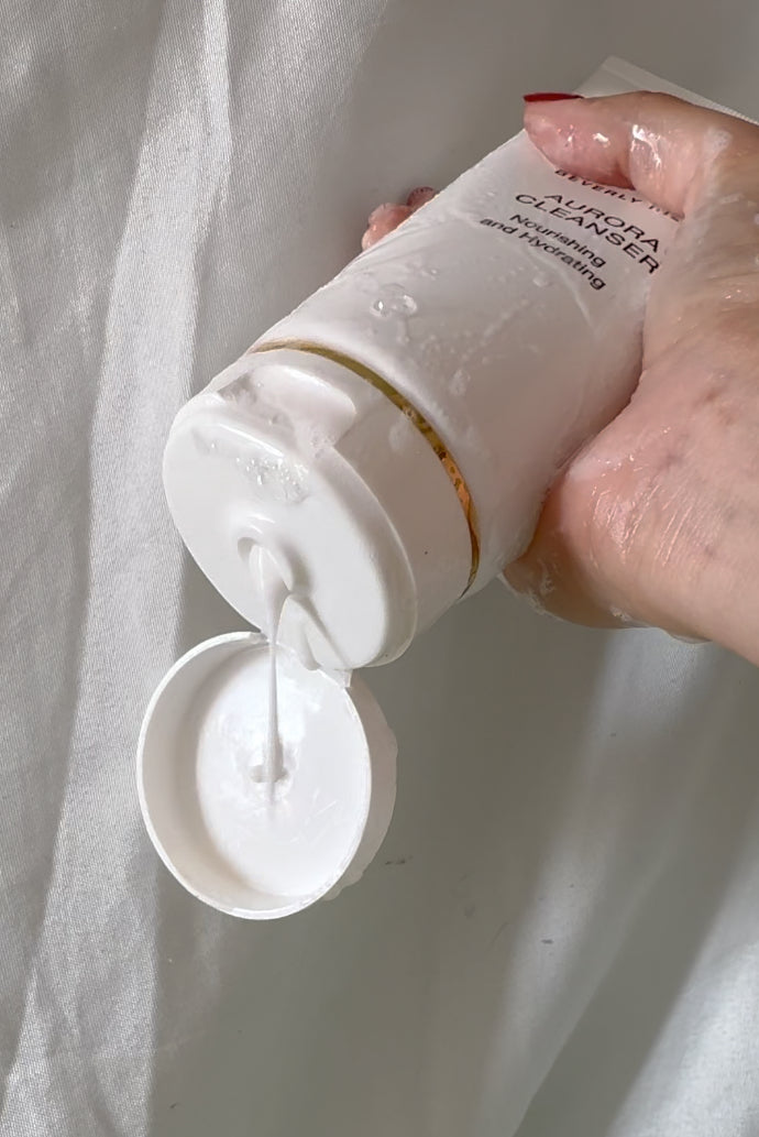 Aurora Cleanser tube held with cap open by EMK Skincare