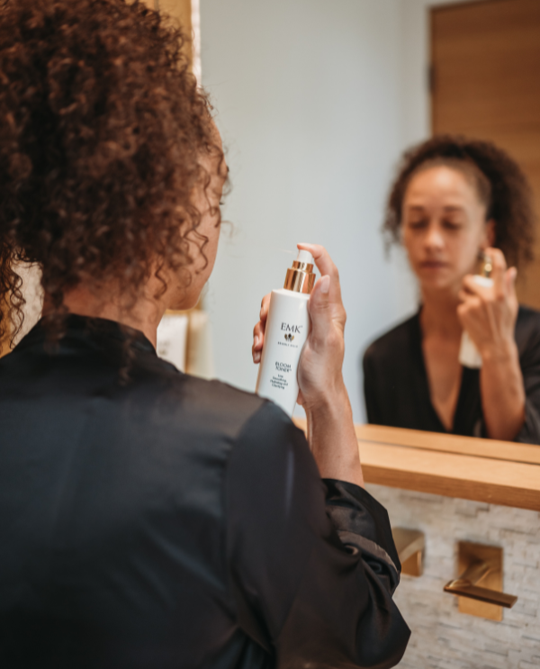 Model applying Bloom Toner in front of a mirror by EMK Skincare