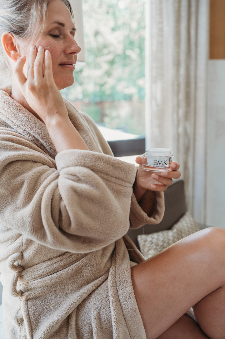 Relaxed model applying Supra Face Cream by a window by EMK Skincare